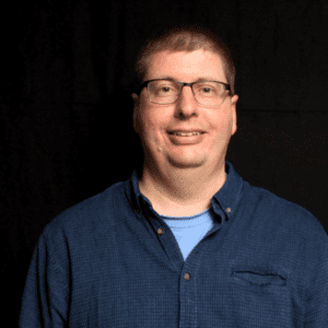 Photo of Bjarne Kallesø smiling in a blue button up shirt and glasses.